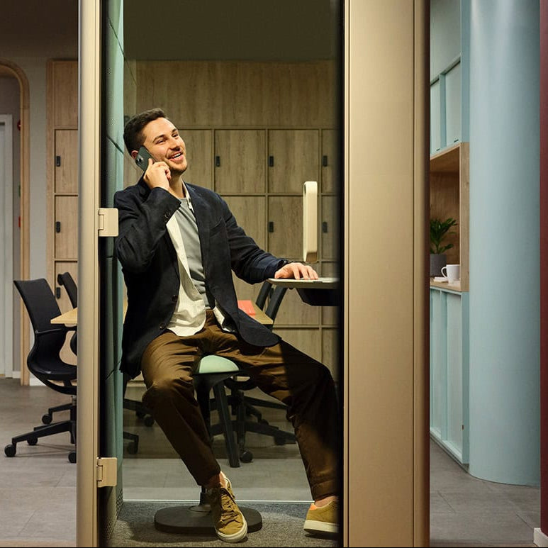 Man talking on a phone in an office setting with colleagues working in the background